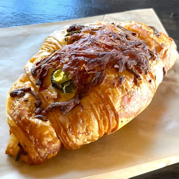 Savory croissant with melted cheese and green peppers on parchment paper from Crave Coffee & Tea.