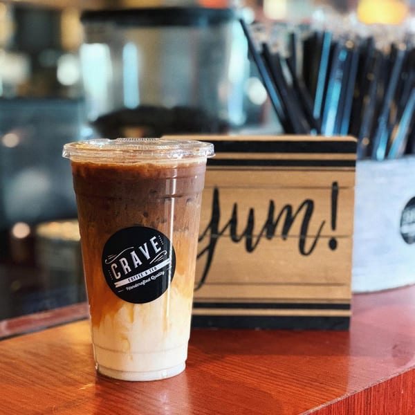 Iced coffee with layers of milk and coffee, featuring a Crave Coffee & Tea logo, on a wooden counter.