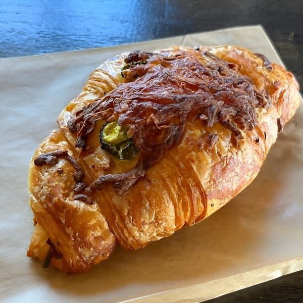 A savory croissant with melted cheese and sliced jalapeños on parchment paper from Crave Coffee & Tea.