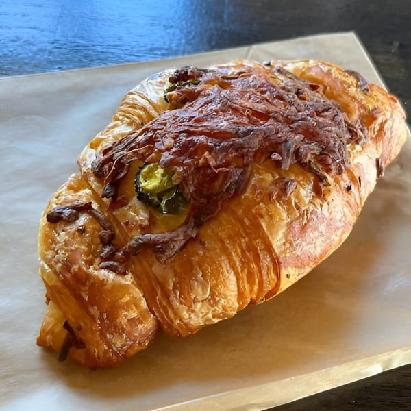 A savory croissant topped with melted cheese and sliced jalapeños on parchment paper.