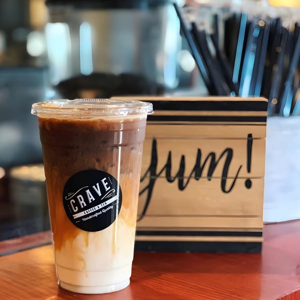 Iced Crave coffee with layered milk and coffee, next to a wooden "Yum!" sign.